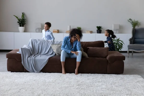Excited hyperactive Black sibling kids running around tired mom — Stok fotoğraf