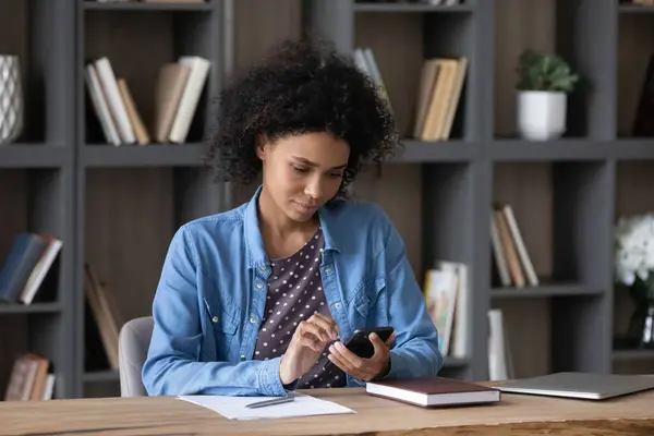 Focused young millennial Black freelance employee woman using smartphone — Stock Photo, Image