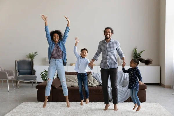 Excited cheerful African parents and little kids jumping on carpet — Stok fotoğraf