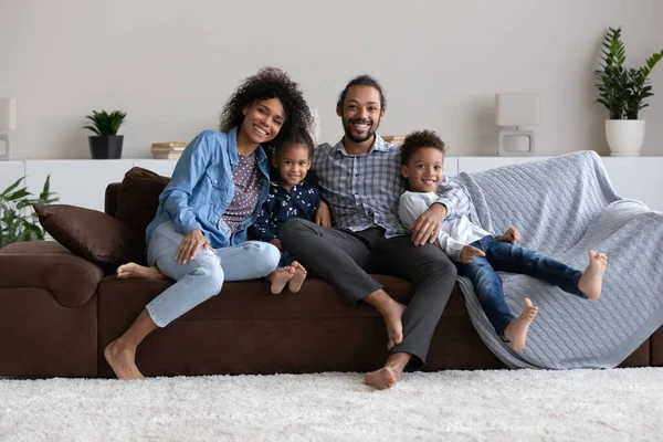 Happy African millennial parents and little children resting on sofa — стокове фото