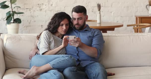 Attractive couple sit on sofa use cellphone, discuss purchase — Vídeos de Stock