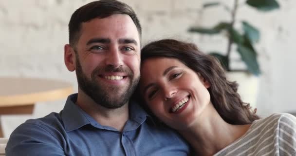 Χαρούμενο ζευγάρι που χαλαρώνει στον καναπέ χαμογελώντας κοιτάζοντας την κάμερα — Αρχείο Βίντεο