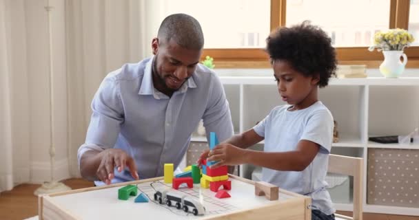 African American father build toy railway station with little son — стоковое видео