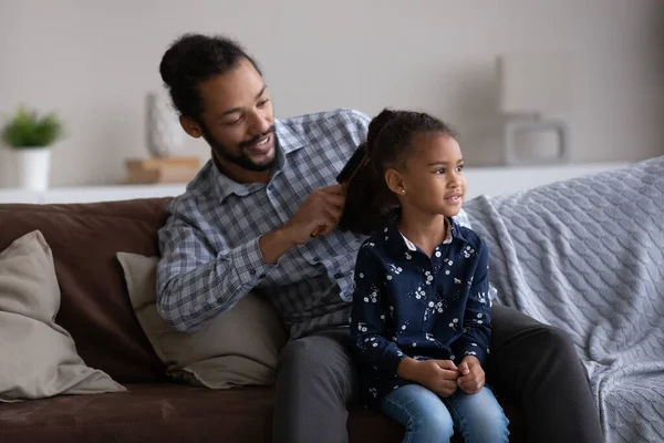 Happy African dad combing curly hair of beautiful little daughter — Foto Stock