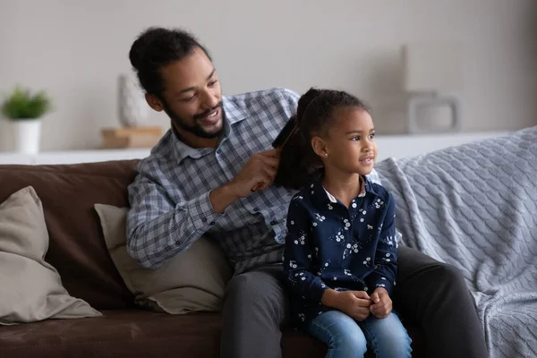 Happy African dad combing curly hair of beautiful little daughter — ストック写真