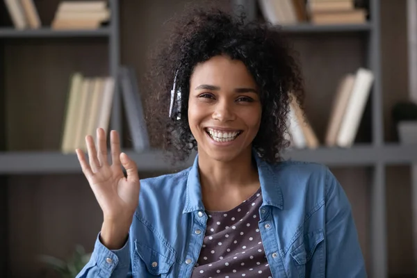 Happy African student, employee in wireless headphones waving hand hello — Stock Photo, Image