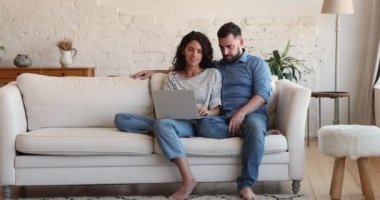 Couple relaxing on couch with laptop, talking discussing purchase on-line