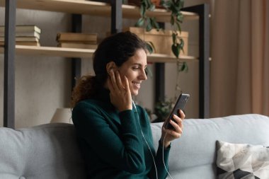 Cheerful young latin hispanic woman in wired earphones using cellphone.