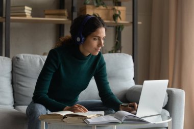 Concentrated smart young woman studying alone at home.
