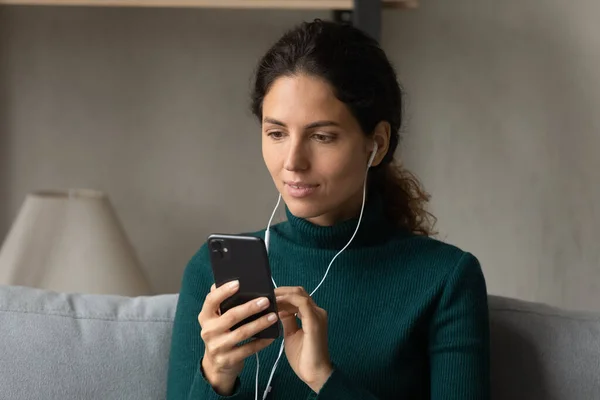 Interested young woman in wired earphones using cellphone. — Stock Photo, Image