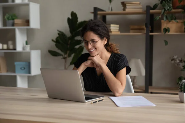 Усміхнена приваблива жінка тисячоліття працює на комп'ютері в домашньому офісі . — стокове фото