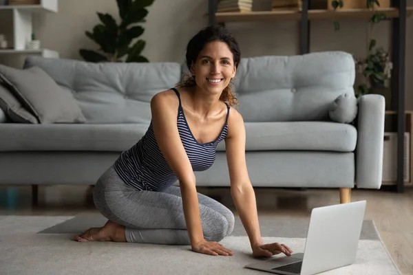 Smiling woman in sportswear sitting on carpet with computer. — Stok fotoğraf