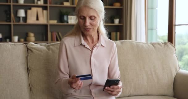 Older woman holds cellphone and credit card buying on internet — Αρχείο Βίντεο