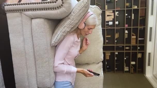 Peaceful senior woman wear headphones relax on sofa with cellphone — стоковое видео