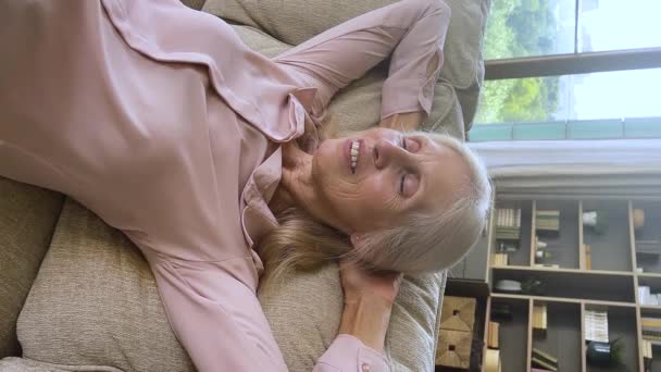 Вертикальний вигляд літня жінка дихає свіжим повітрям, розслабляючись на дивані — стокове відео