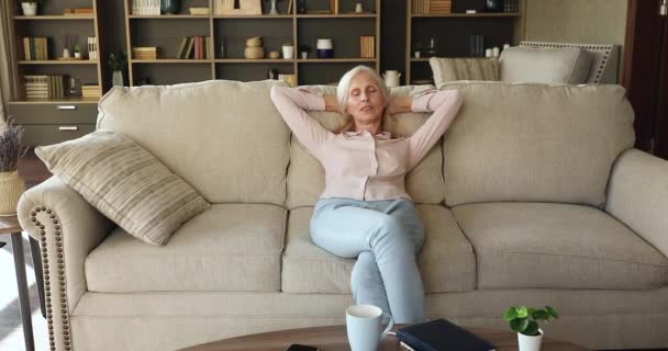 Безтурботний літня жінка насолоджується розслабляючим сидінням на дивані вдома — стокове відео