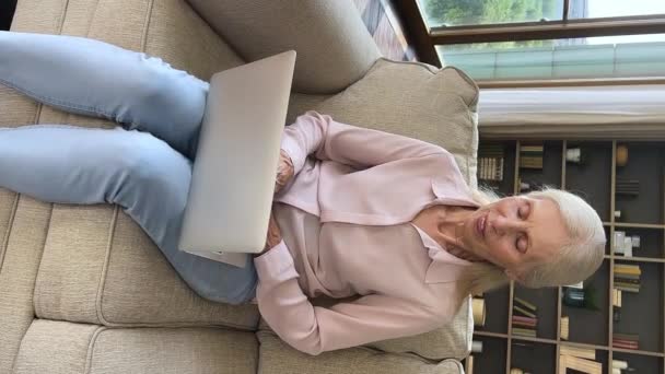 Vertical view mature woman sit on sofa texting on laptop — 비디오