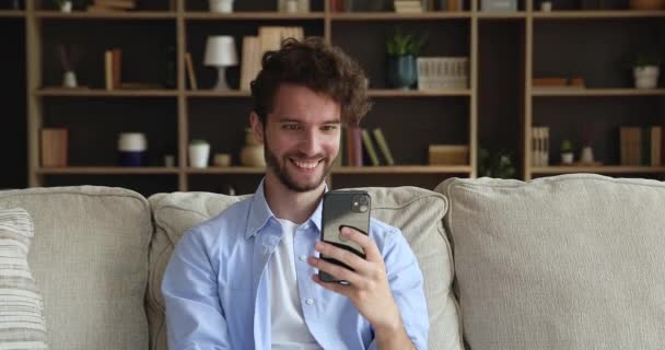 Guy sit on sofa looks at cellphone screen read news — ストック動画