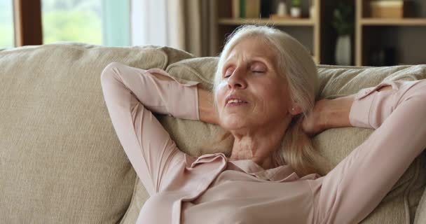 Крупним планом мирна літня жінка насолоджується денним відпочинком лежачи на дивані — стокове відео