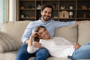 Happy spouses relaxing on sofa smile look at camera