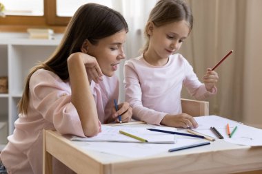 Young mother and daughter holding colourful pencils painting on paper album