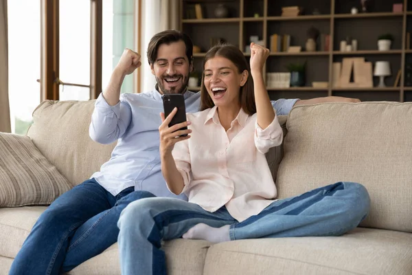 Overjoyed couple sit on sofa with cellphone celebrate bet victory — Stockfoto