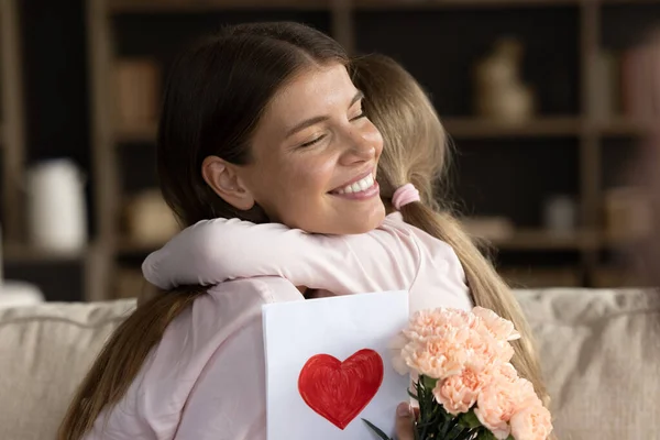 Mujer sostiene postal y ramo abrazando a su pequeña hija — Foto de Stock