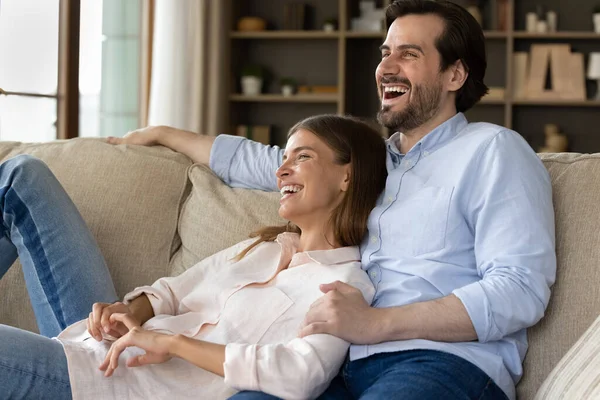 Pareja relajándose en el sofá riendo pasar un fin de semana sin preocupaciones en casa — Foto de Stock