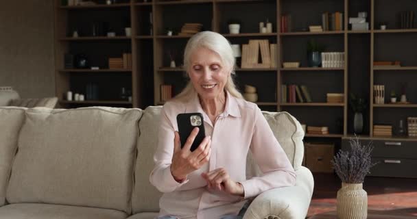 Senior woman sit on holds smartphone talk on video conferencing — Stock video