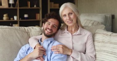 Older mum adult son relax on sofa look at camera