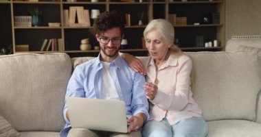 Adult son his older mum sit on sofa with laptop