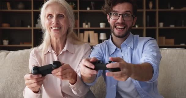 Mature grandmother and adult grandson having fun play racing videogames — Stockvideo