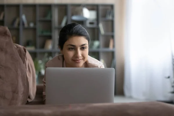 Pleasant happy young Indian woman using computer, resting on sofa. — Stock Photo, Image