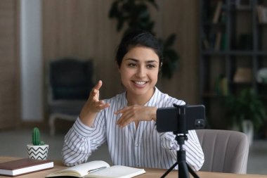 Smiling young Indian businesswoman recording video on cellphone.