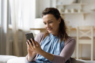 Beautiful smiling millennial woman using cellphone at home.