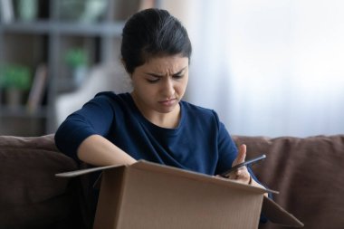 Stressed young Indian woman unpacking carton box.
