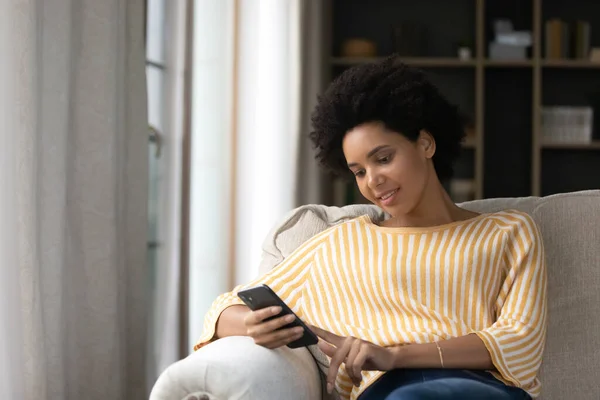 Ontspannen jonge Afro-Amerikaanse vrouw met behulp van mobiele telefoon. — Stockfoto
