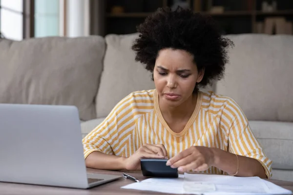 Unhappy stressed young African American woman managing monthly budget.
