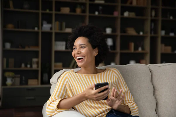 Laughing young woman using cellphone at home. — Stockfoto
