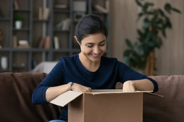 Curious smiling millennial Indian woman unpacking carton box. — Photo