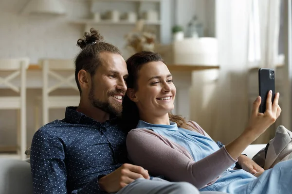 Joyful affectionate young family couple using cellphone at home. — Stockfoto