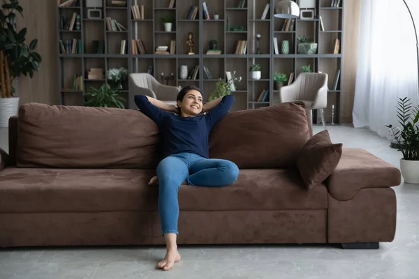 Happy young female Indian homeowner resting on sofa. — Stockfoto