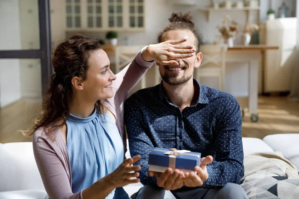Caring cheerful young woman giving gift box to joyful husband. — Stock fotografie