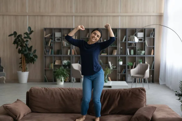 Happy energetic young Indian woman jumping barefoot on cozy sofa. — Stok Foto