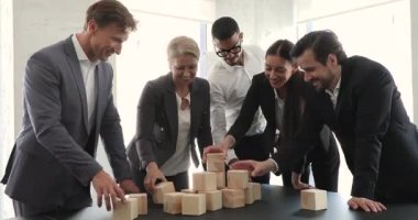 Five businesspeople engaged in teambuilding, build tower using wooden cubes