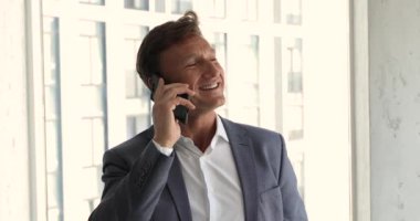 Businessman in suit stands in modern office talks on smartphone