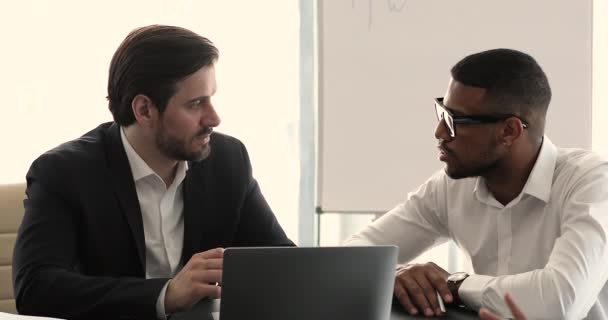 Two multiethnic colleagues discuss business sit at desk in office — Vídeos de Stock