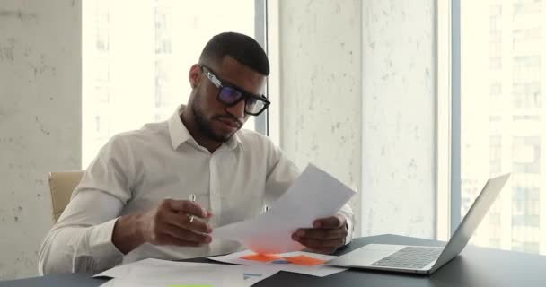 African businessman sit at workplace desk use laptop, examining document — Stock Video