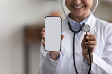 Close up smiling young Indian doctor advertising mobile healthcare apps.
