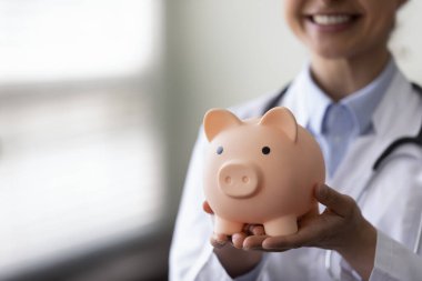 Close up young Indian doctor holding piggybank in hands.